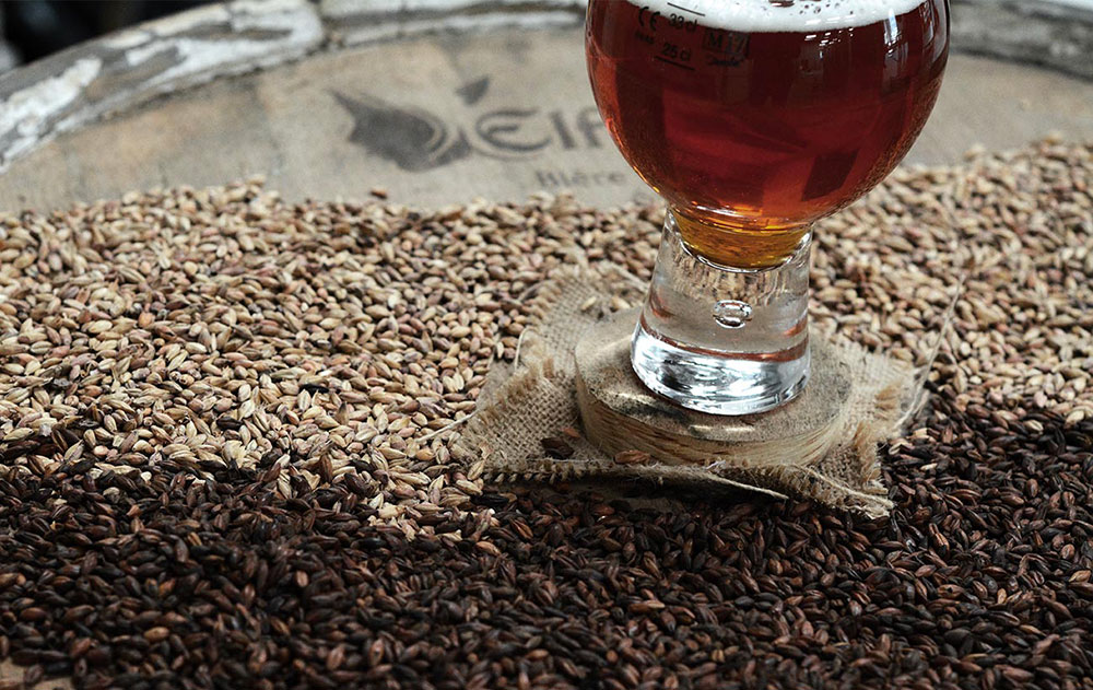 A glass of Elfique on some barley on top of a wooden barrel