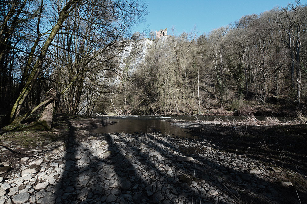 Une rivière en fôret, surplombé par une ruine sur une falaise